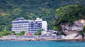 Ein Gebäude an der Küste mit mehreren Stockwerken, nahe einer felsigen Klippe und eines Gewässers.