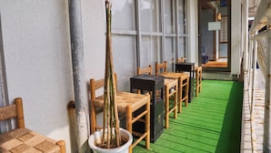 Un couloir avec des chaises et des tables, une plante en pot et un sol recouvert d’un gazon artificiel vert.