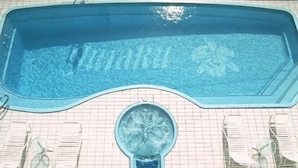 Une piscine avec un jacuzzi central, une terrasse carrelée et des chaises longues.