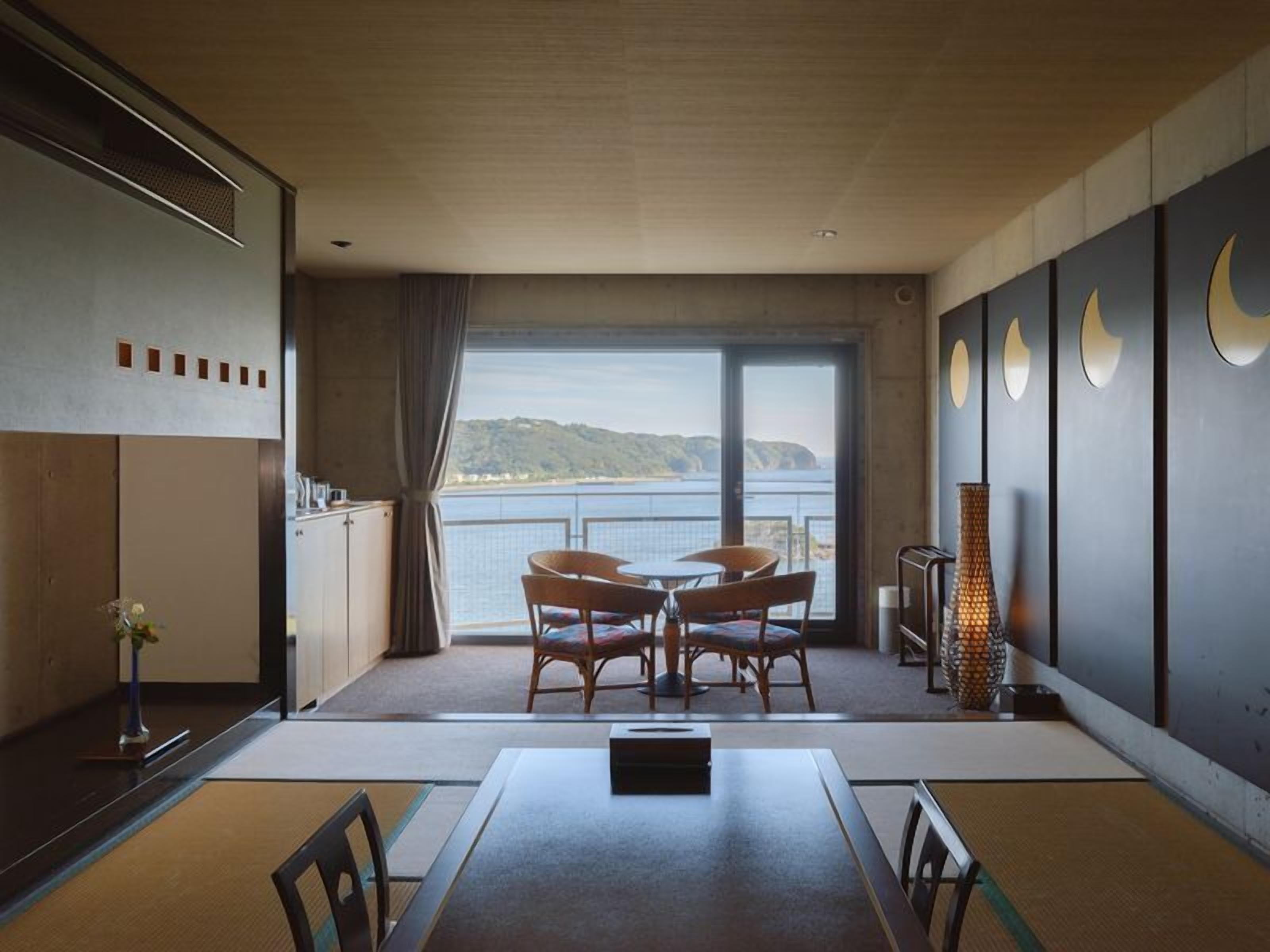A modern room with a dining table, chairs, a vase, and a view of the sea.