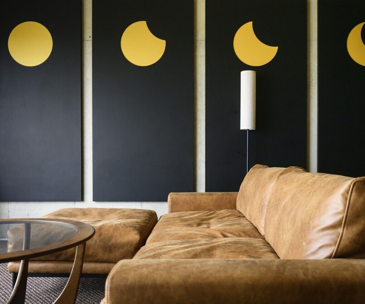 A modern living room with a leather sofa, a glass coffee table, and a wall with abstract yellow and crescent moon decorations.