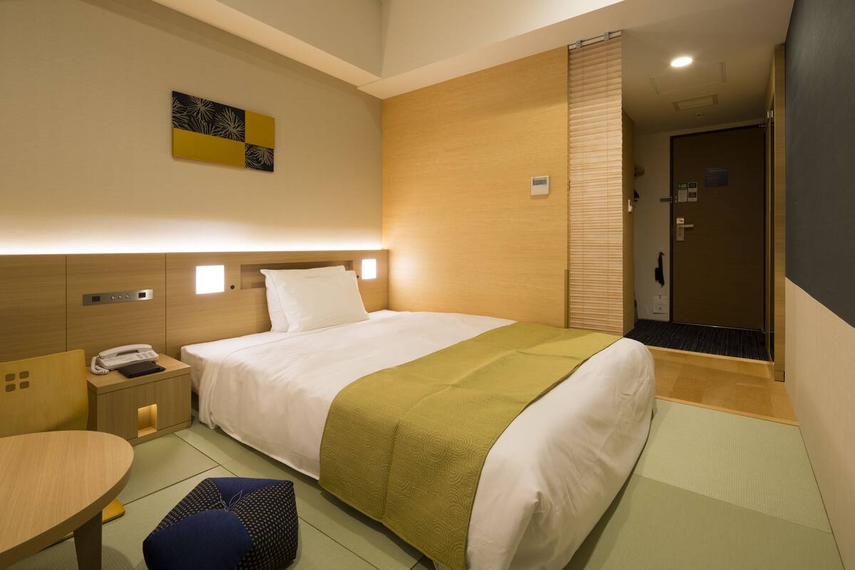 Una habitación de hotel con una cama, mesita de noche y un escritorio pequeño con una silla.