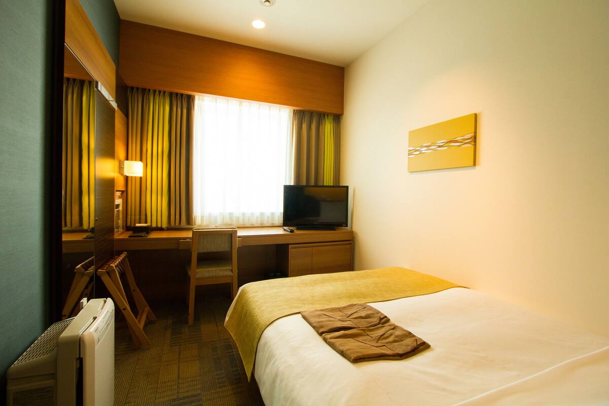 Una habitación de hotel con cama, escritorio, silla, televisión y un cuadro en la pared.