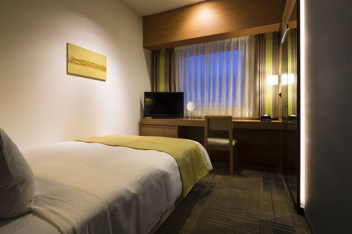 Una habitación de hotel con dos camas, un escritorio con televisor y una ventana con cortinas.