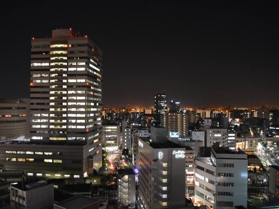 A nighttime cityscape with high-rise buildings, illuminated windows, and a busy street.