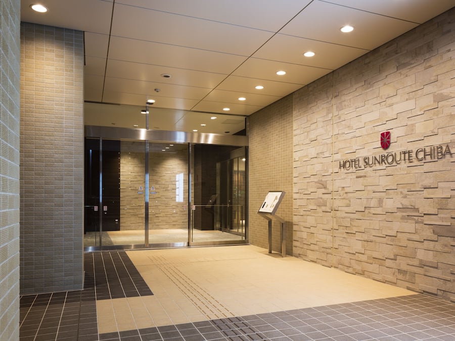 A hotel entrance with a modern design, featuring a brick wall and a glass door leading to the lobby.