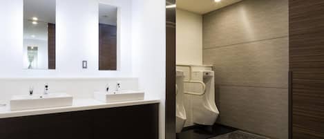 A modern bathroom with two sinks, a large mirror, and a urinal.