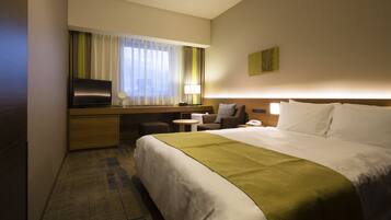 A hotel room with a large bed, a desk with a TV, a small table, and a chair.