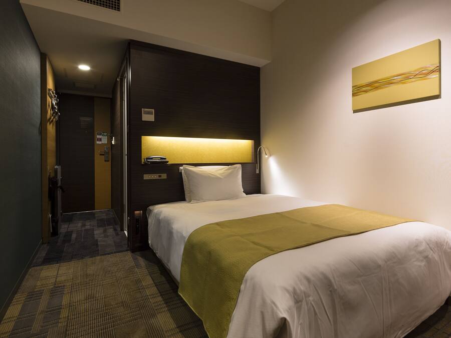 Habitación de hotel con cama, mesita de noche, lámpara y un cuadro en la pared.