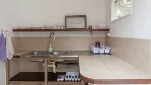 Een kleine keuken met een spoelbak, een plank met servies en een klein raam.
