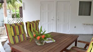 Een houten tafel met gestreepte stoelen, een vaas met bloemen en een witte deur op de achtergrond.