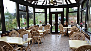 A conservatory with wicker furniture, large windows, and a tiled floor. - The Golden Larches Cafe and B&B (Lochearnhead)