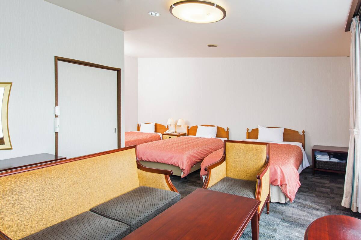 A hotel room with two single beds, a sofa, a table, and a chair.
