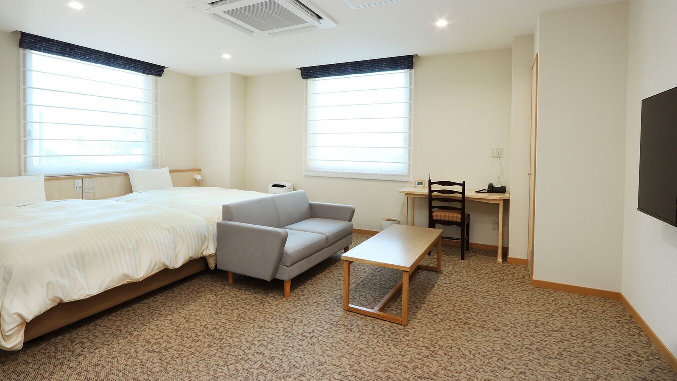 A hotel room with a bed, a sofa, a small table, and a desk with a chair.