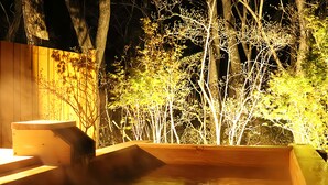 Una terrazza in legno con una vasca idromassaggio, circondata da alberi e un recinto in legno.