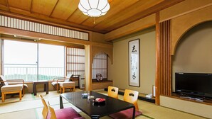 Una camera in stile tradizionale giapponese, con pavimento in tatami, un tavolino con cuscini, una televisione e una porta scorrevole.