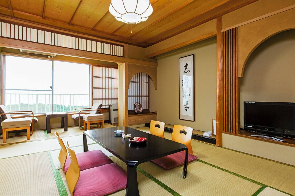 A traditional Japanese-style room with tatami flooring, a low table with cushions, a television, and a sliding door.