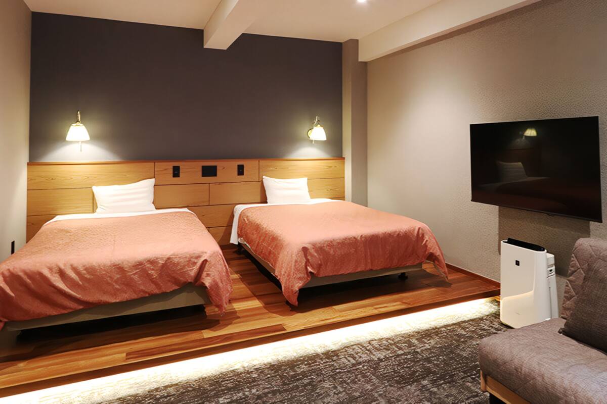 A hotel room with two beds, a TV mounted on the wall, and a wooden floor.