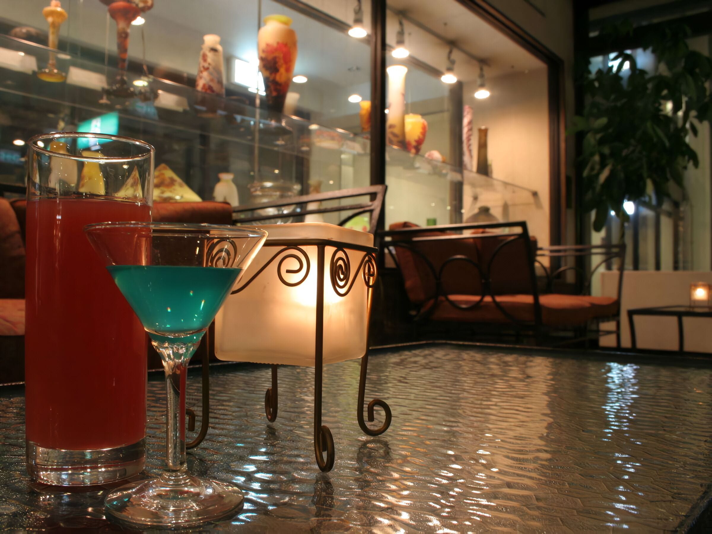 Una zona de bar con una mesa de cristal, dos cócteles y una lámpara decorativa.