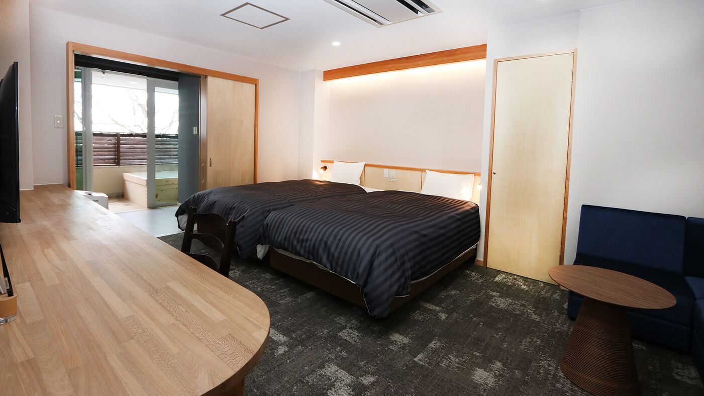 A hotel room with a bed, a desk, a chair, a small table, and a sofa.