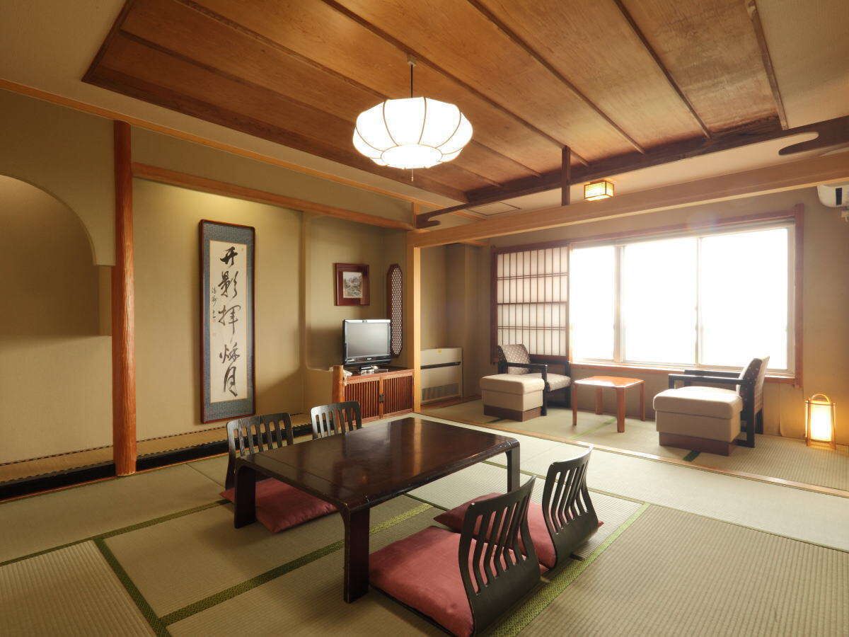 A traditional Japanese room with tatami flooring, a low table with cushions, a television, and a sliding door.