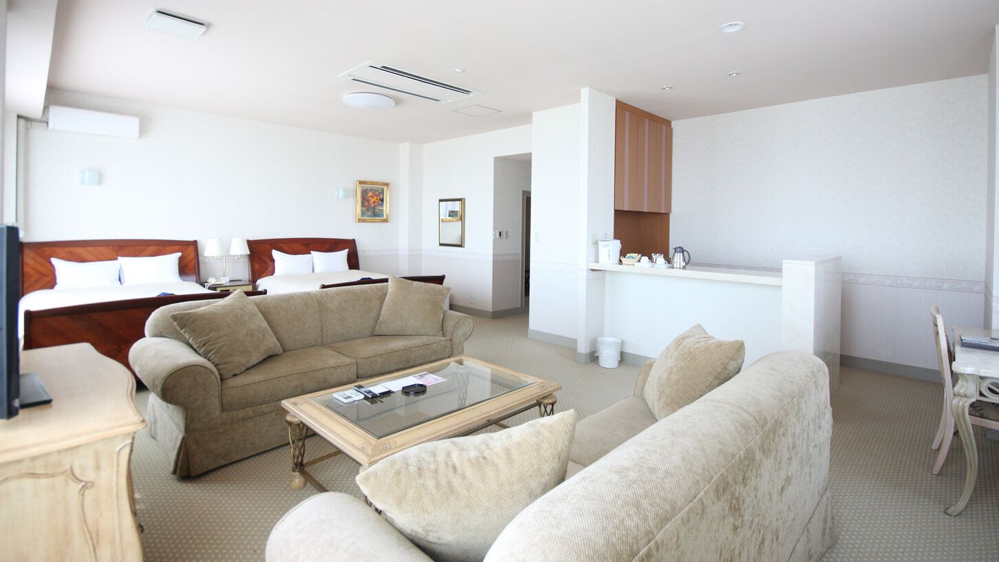 A hotel room with a bed, two sofas, a coffee table, a TV, a kitchen area, and a dining table.