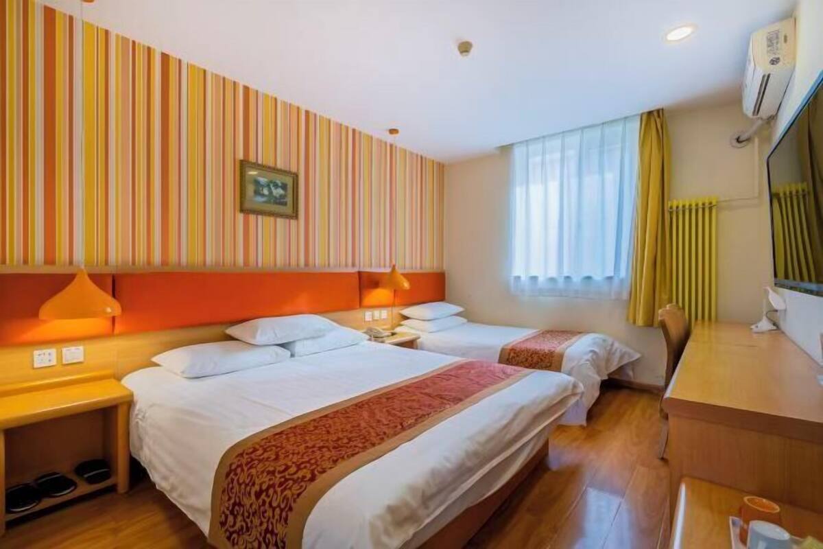 A hotel room with two beds, a desk, and a window with curtains.