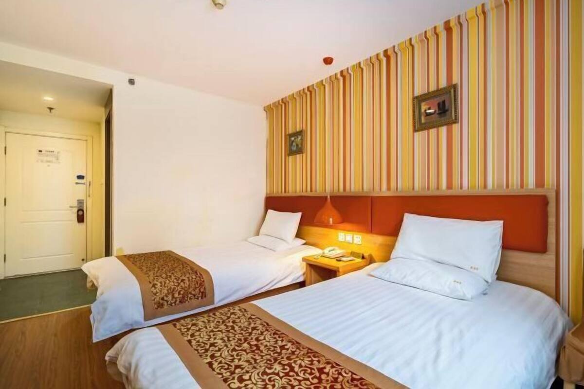 A hotel room with two beds, a striped wall, a wooden headboard, and a bedside table with a lamp.