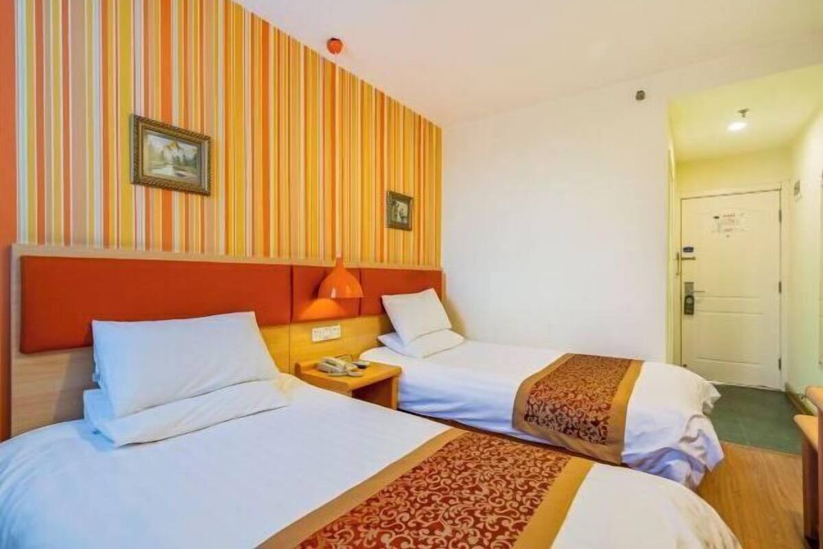 A hotel room with two beds, striped wallpaper, a headboard, a nightstand, and a door.