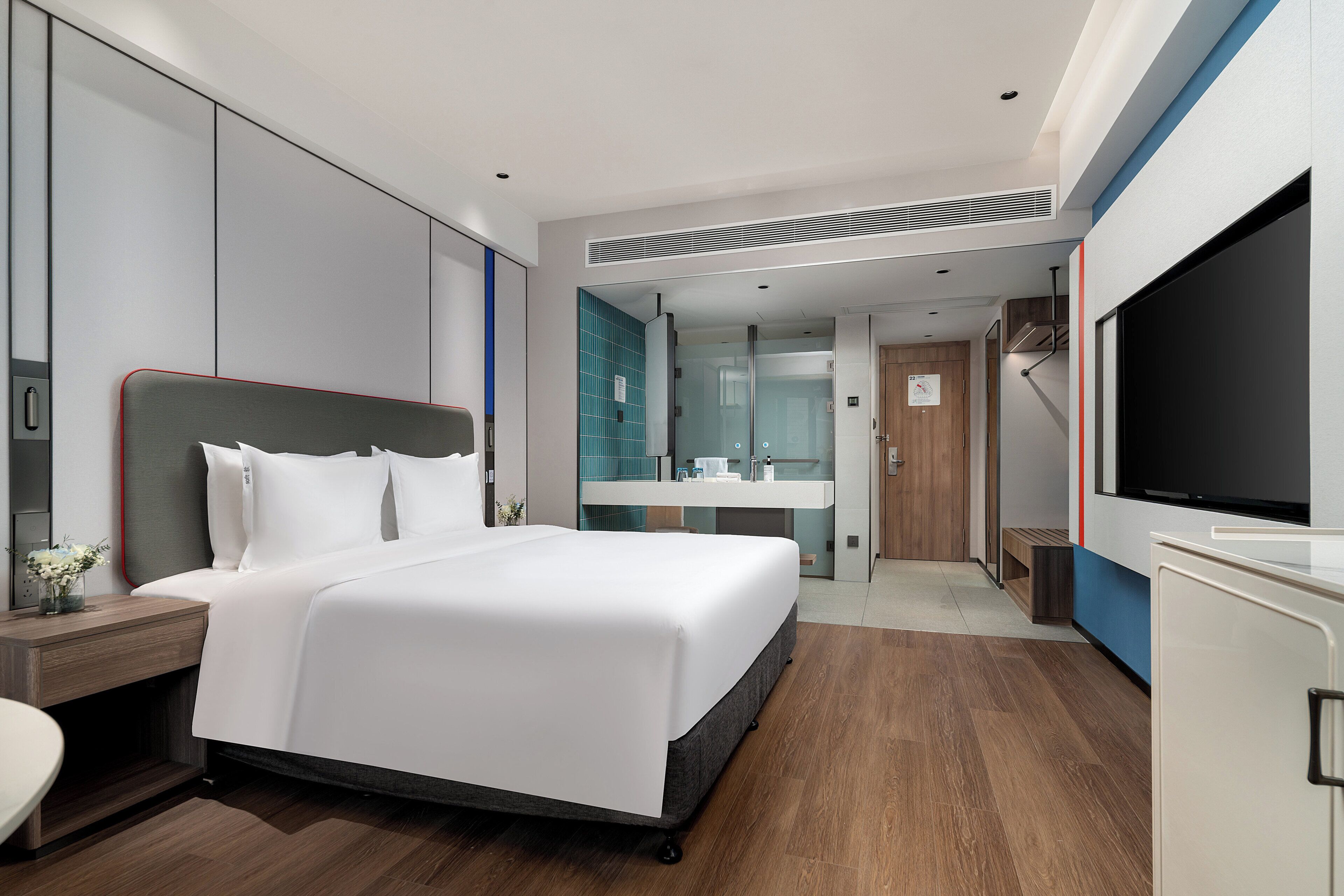 A modern hotel room with a large bed, a bedside table, a TV, and a bathroom with a mirror and sink.