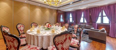 Une salle à manger élégante, avec une table ronde dressée pour le repas, entourée de chaises richement décorées.