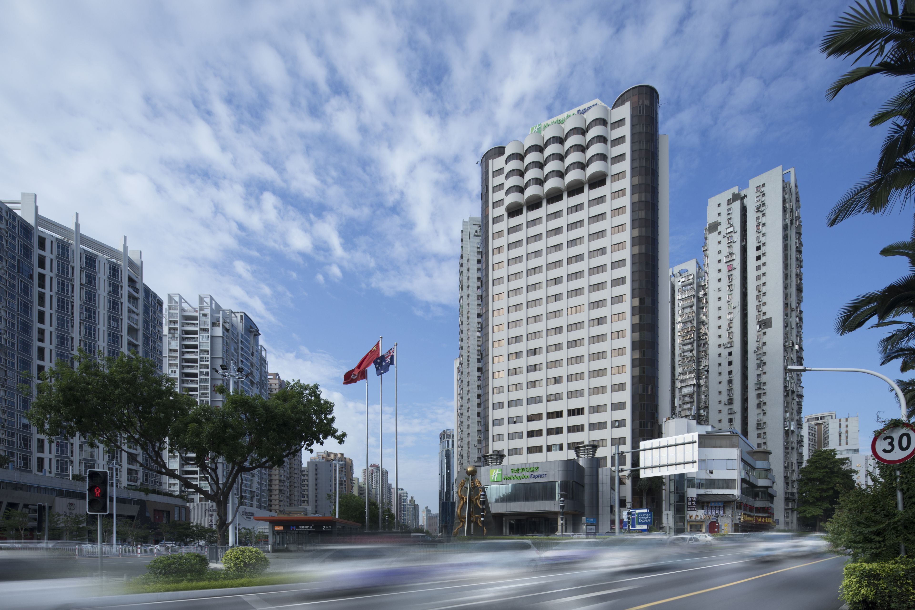 A modern urban street with high-rise buildings, a traffic light, and a speed limit sign.