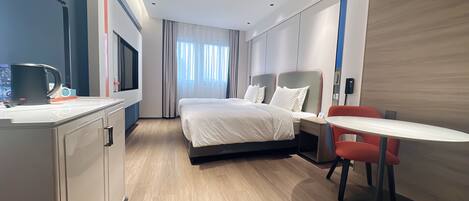 A modern hotel room with a bed, bedside table, and a small desk with a chair.
