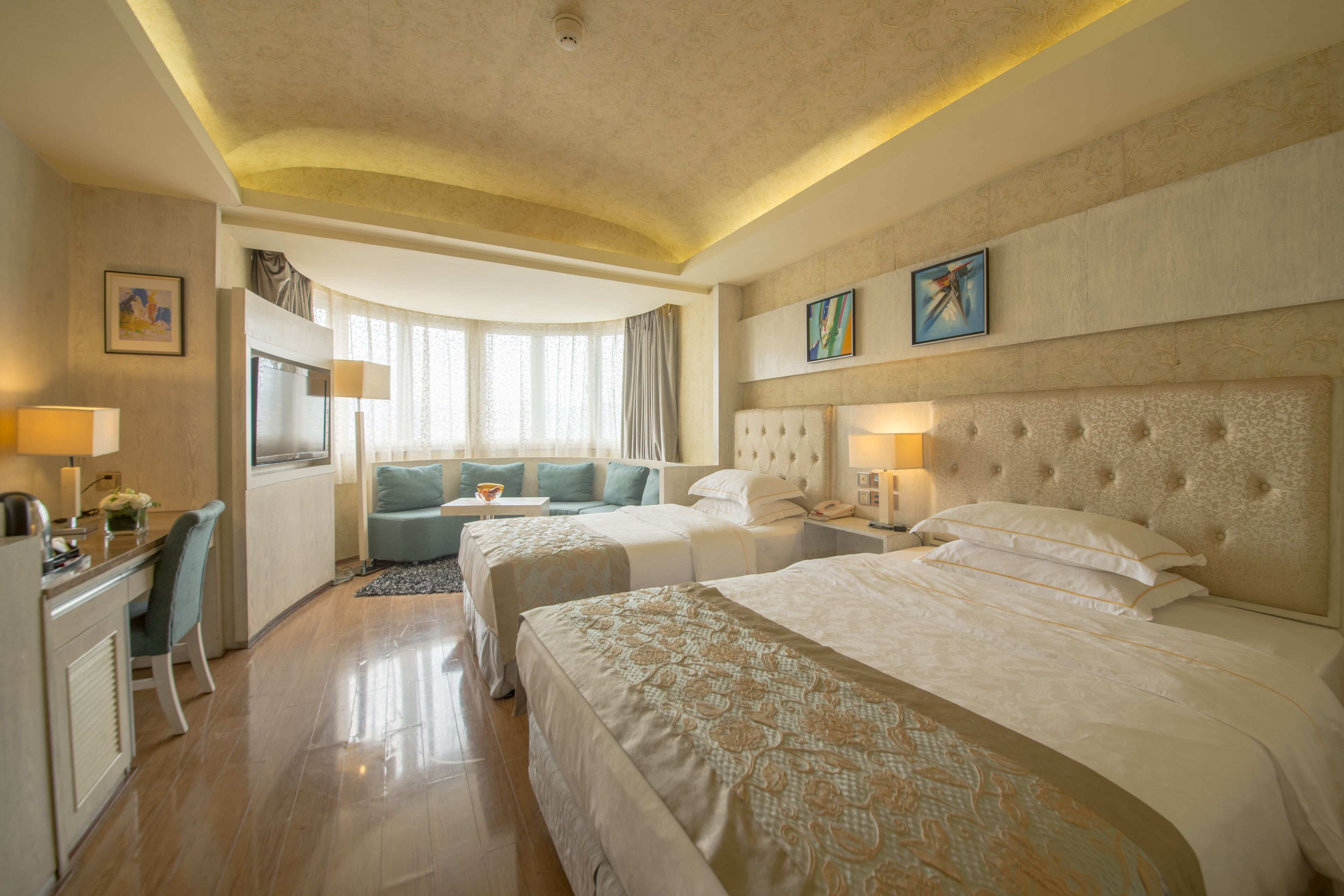 A hotel room with two beds, a desk, a sofa, and a dining area.