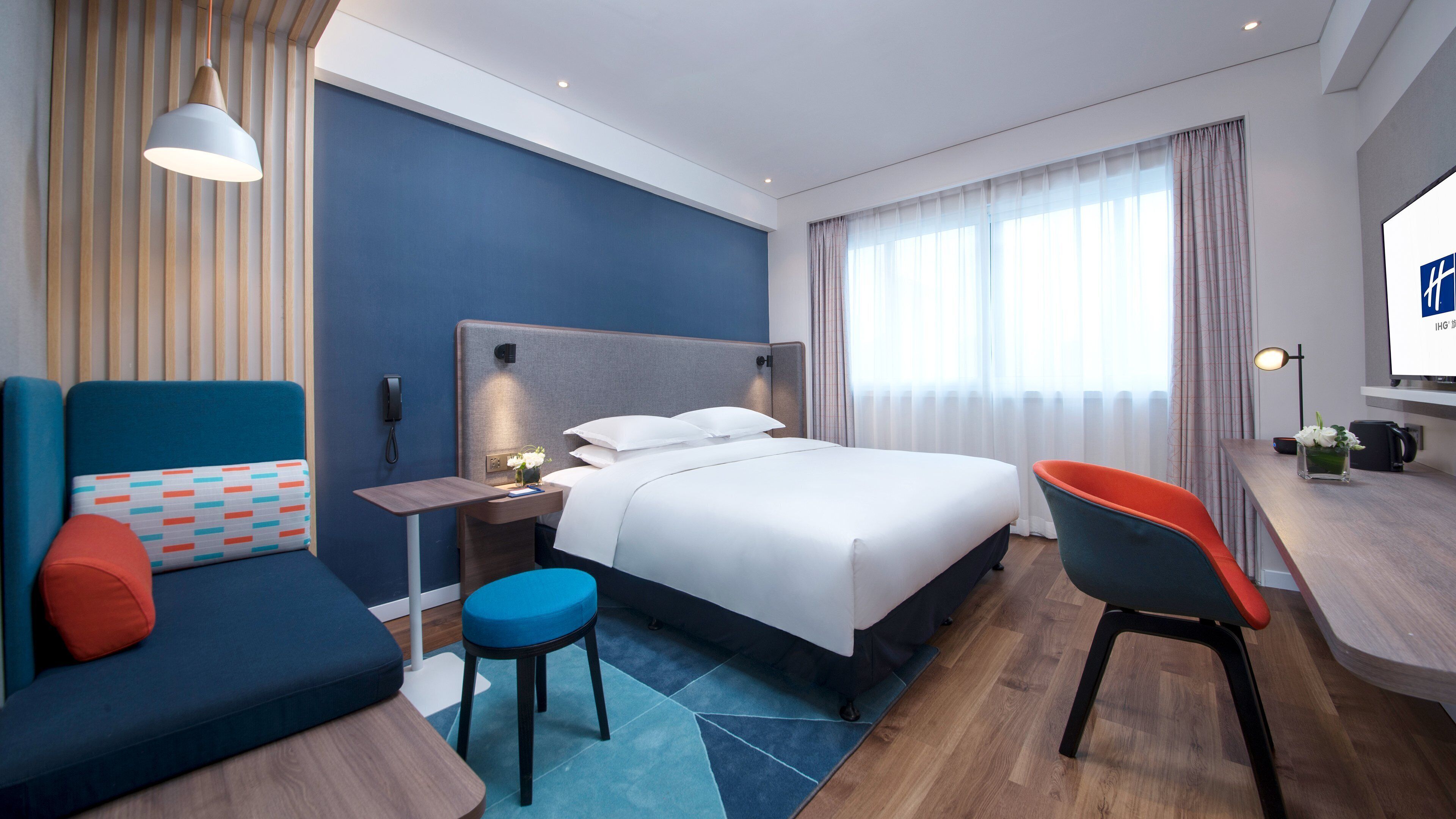 A modern hotel room with a bed, a desk, a chair, a sofa, and a small table.