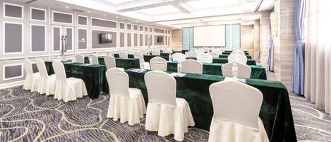 A conference room with rows of tables, white chairs, and a large screen.