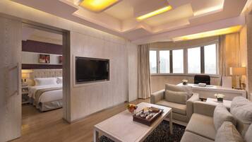 A modern hotel room with a bed, a flat-screen TV, a sofa, a coffee table, and a large window offering a city view.
