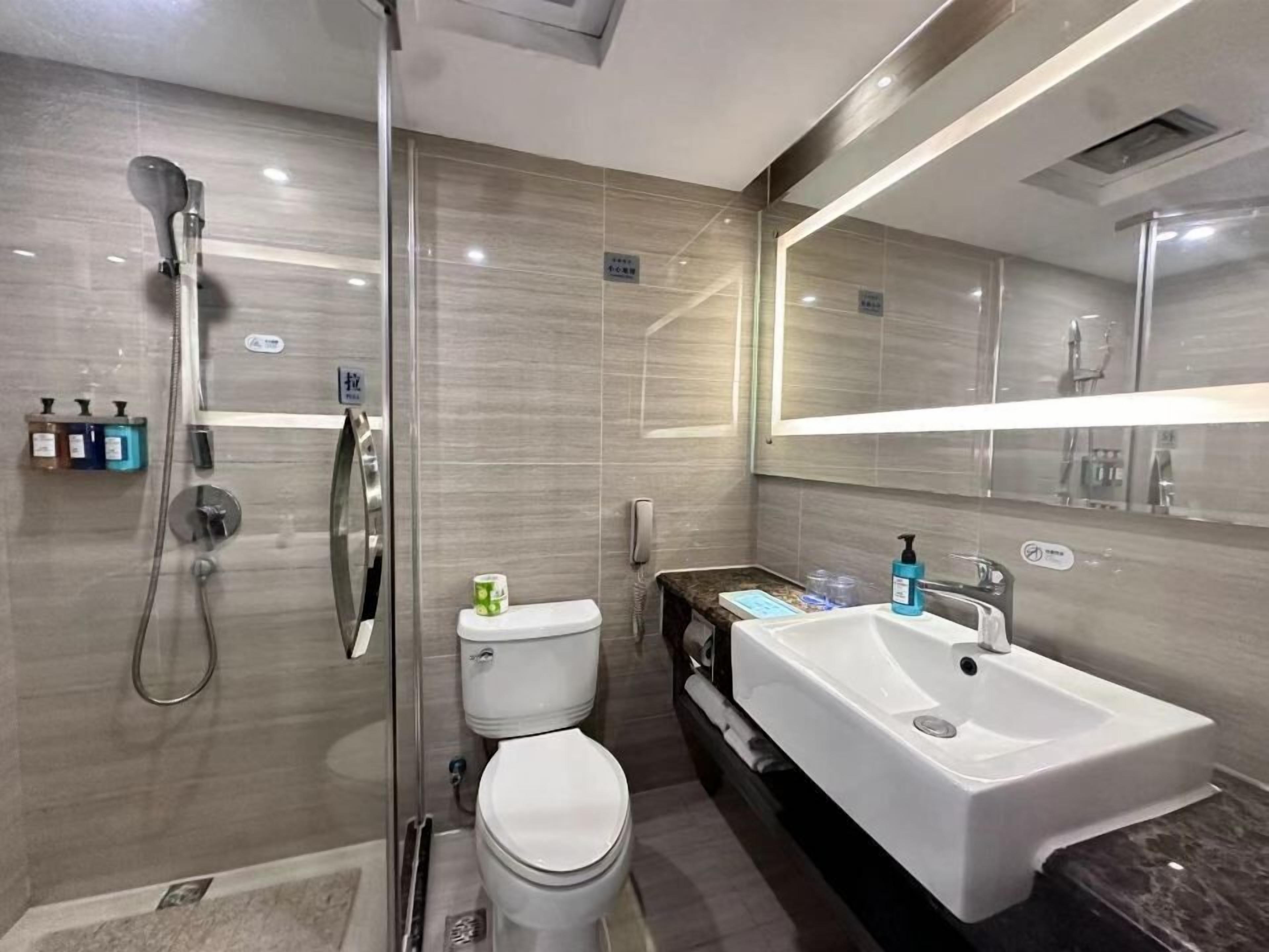 Et moderne badeværelse med et glasvægshus, et hvidt toilet, en stor vask og et spejl over vasken.