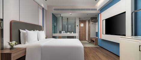 Una habitación de hotel moderna con una cama grande, televisión, escritorio y baño visible a través de una puerta abierta.