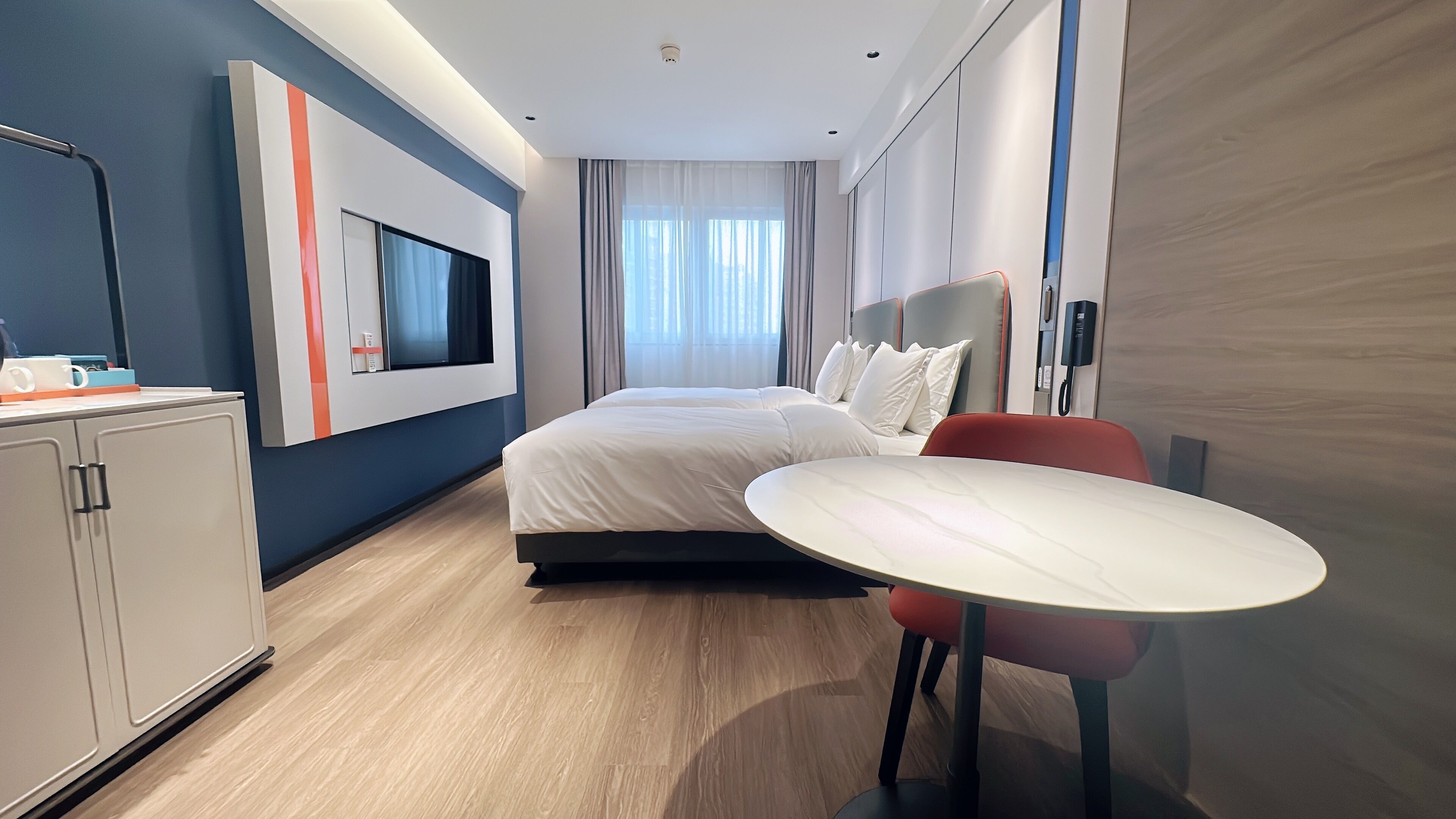 Een moderne hotelkamer met een bed, bureau, stoel, televisie en minibar.