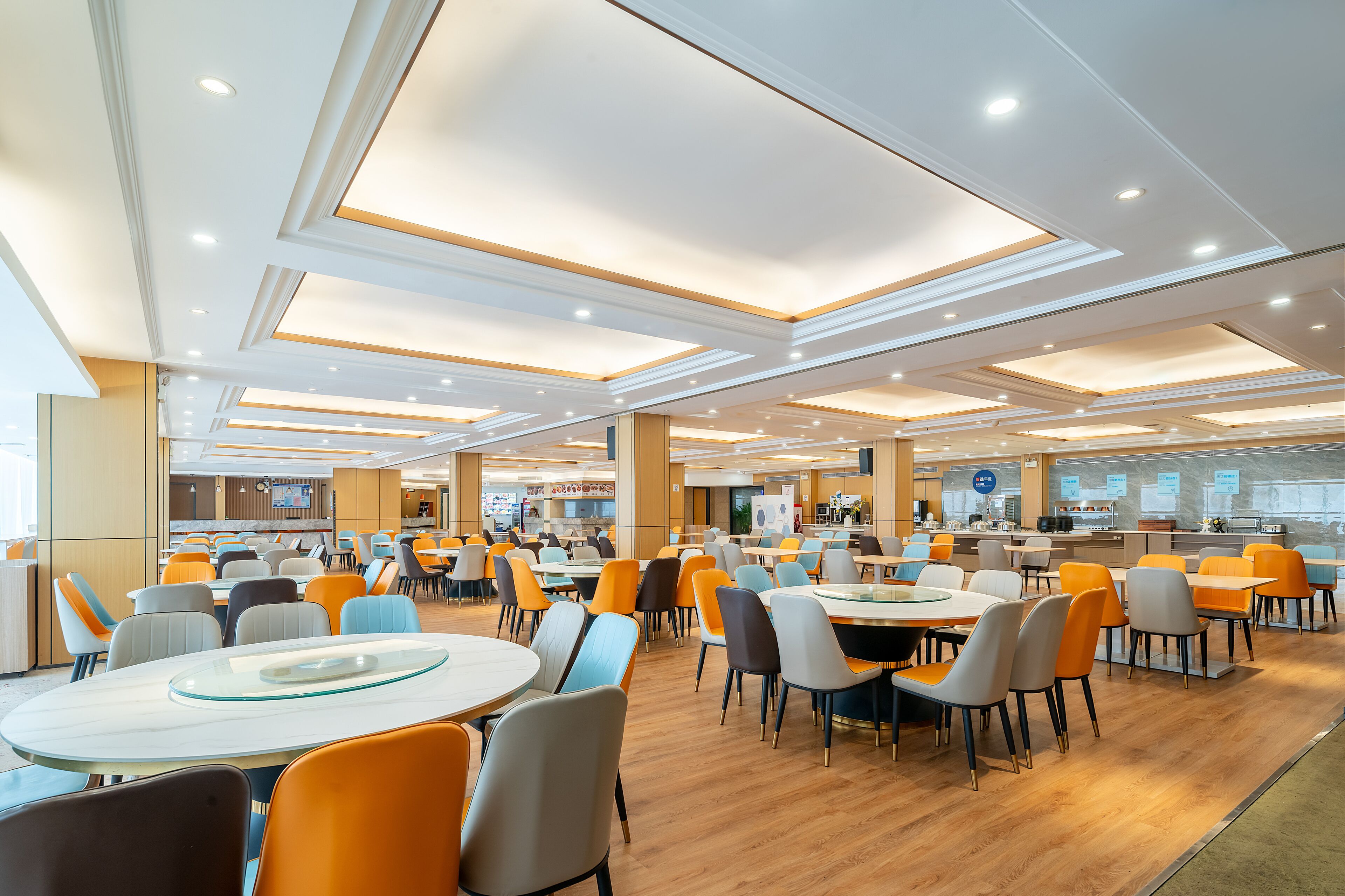 A spacious cafeteria with multiple tables and chairs, a kitchen area, and a counter with a menu display.