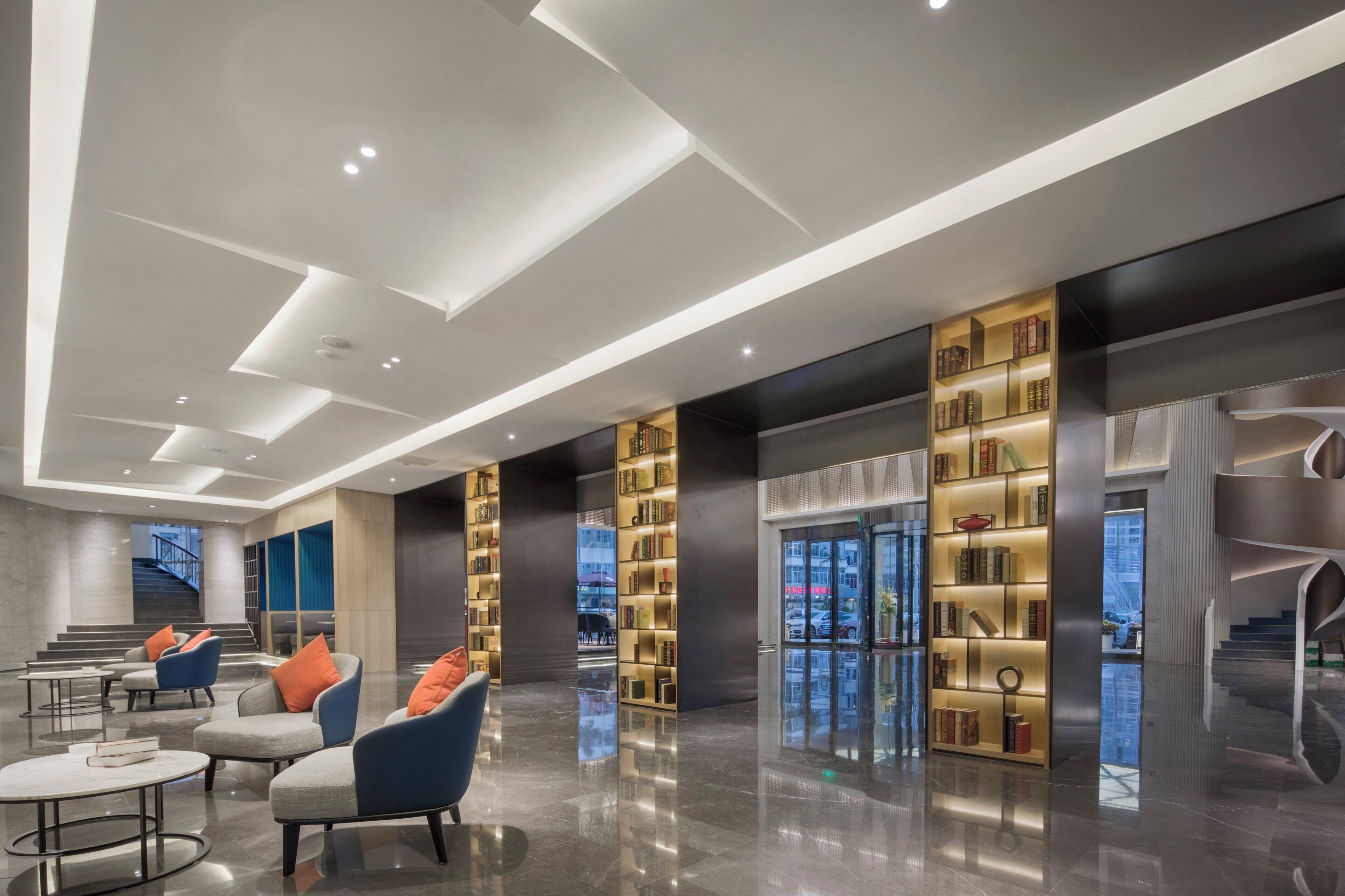 A modern lobby with seating, bookshelves, and a staircase.