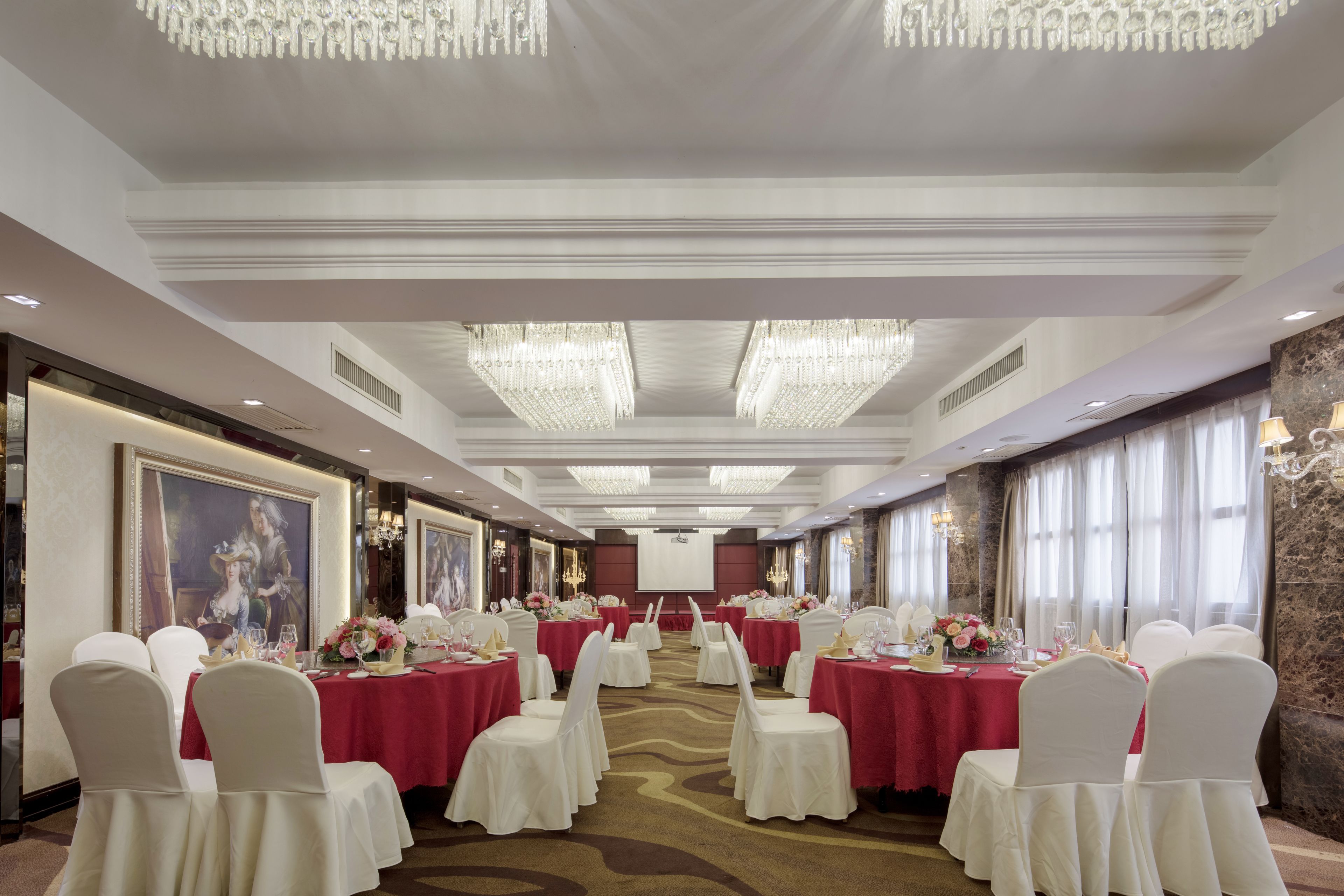 A banquet hall with round tables, white chairs, and red tablecloths.