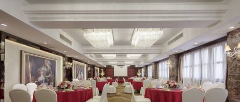 A banquet hall with round tables, white chairs, and red tablecloths.