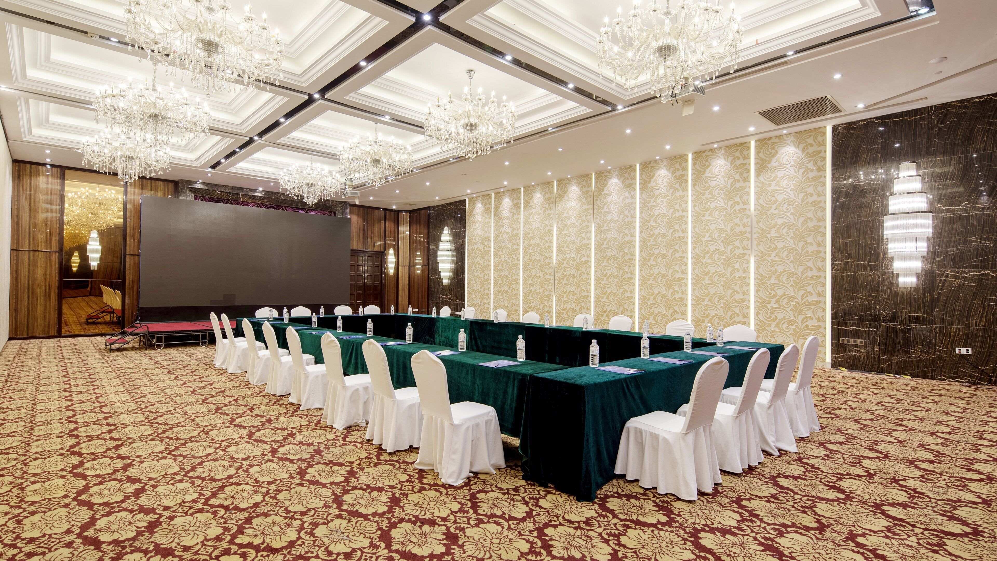 A conference room with a long table, white chairs, and a large screen.