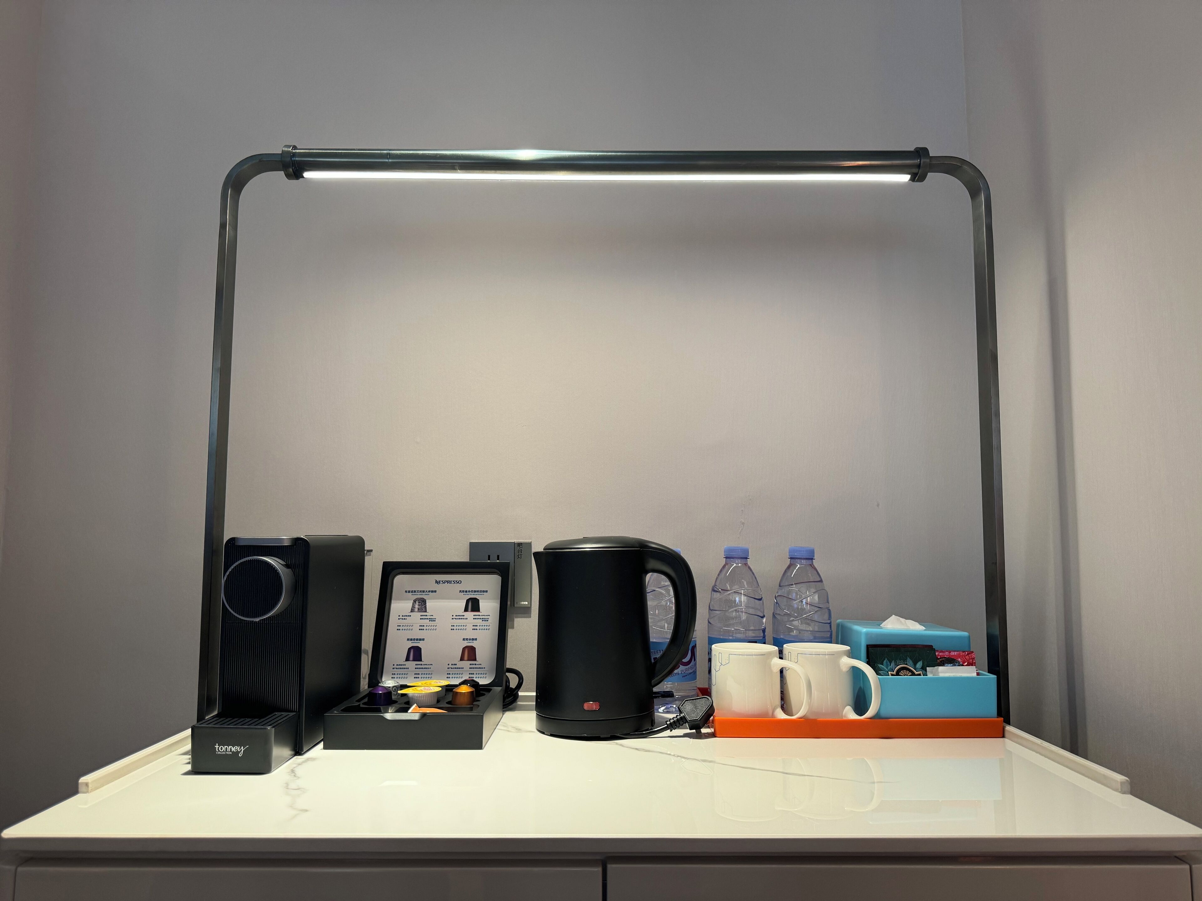 A desk with a coffee maker, a kettle, two water bottles, and a mug holder.