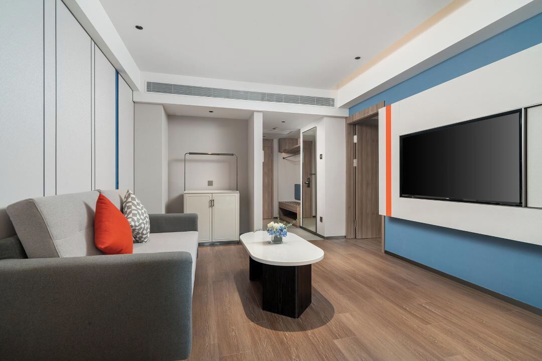A modern living room with a grey sofa, a coffee table, and a flat-screen TV mounted on the wall.