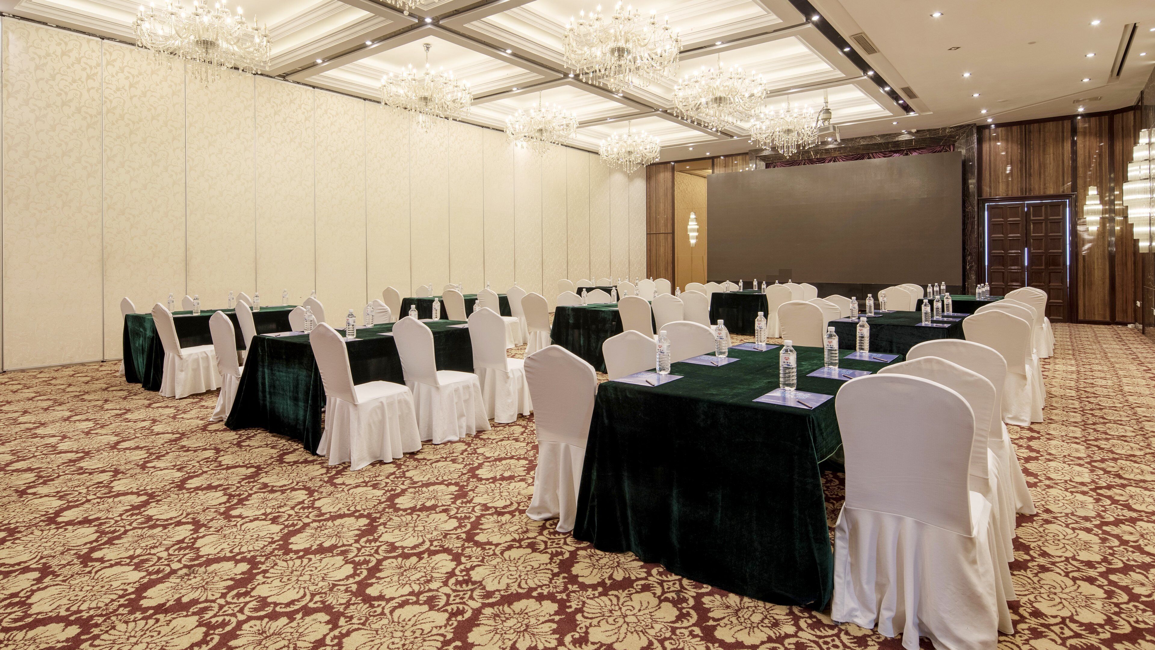A conference room with multiple tables, white chairs, and a carpeted floor.