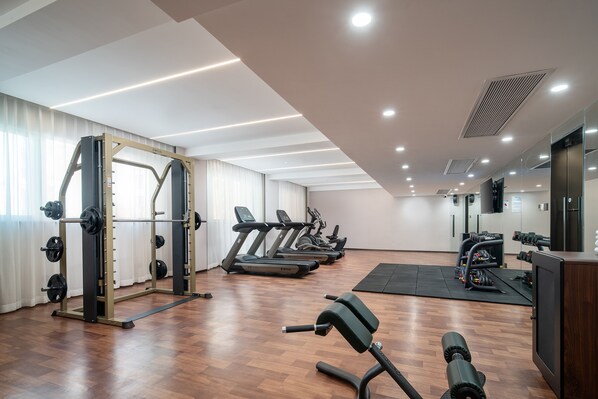 Un gimnasio con cintas de correr, una estructura para sentadillas y equipamiento de levantamiento de pesas.