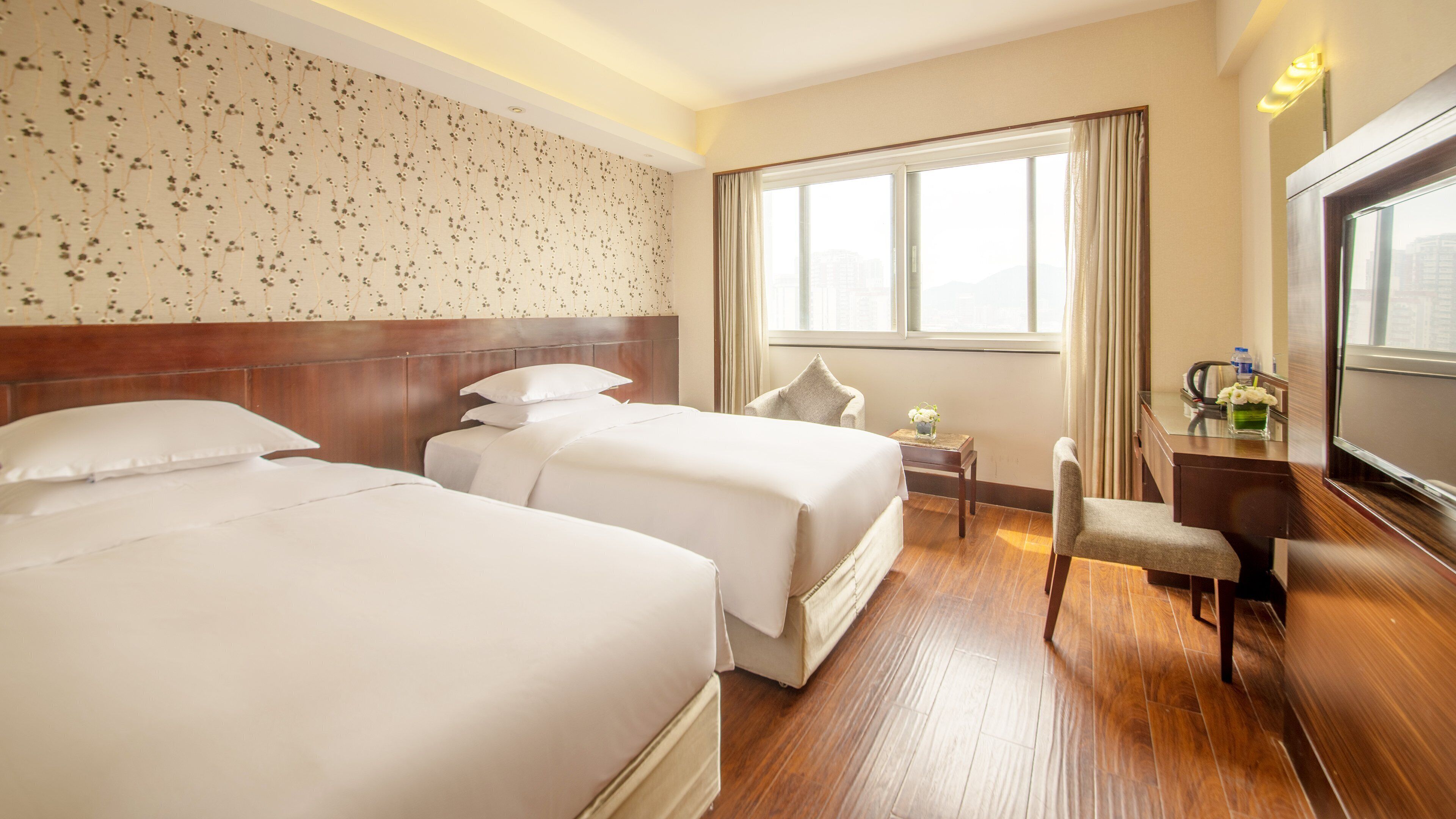 A hotel room with two beds, a desk, a chair, and a large window.